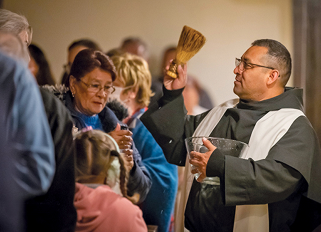 el Padre Juan Zúñiga, O.F.M.Conv. bendiciendo a los fieles con agua bendita.